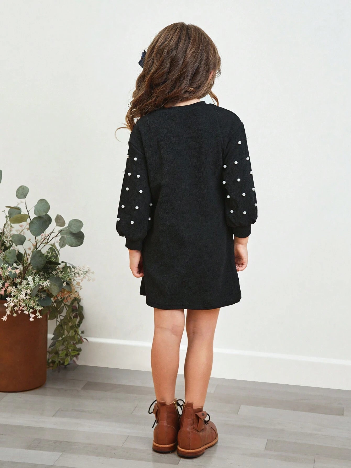 Vista trasera del vestido negro para niñas con corte recto y mangas largas decoradas con perlas.