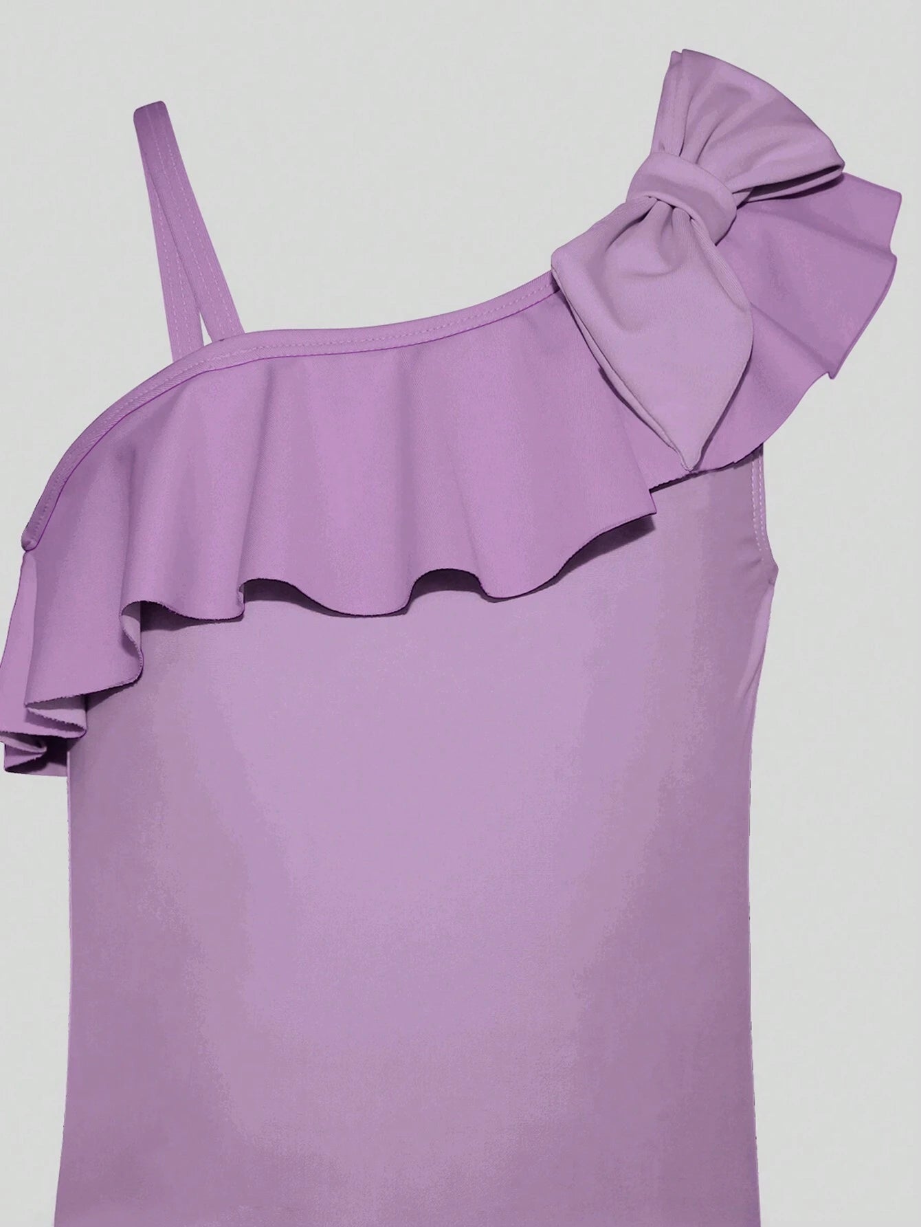 Detalle del volante y lazo en el traje de baño morado, resaltando el diseño femenino y elegante.