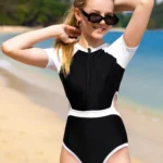 Niña posando en la playa con traje de baño deportivo blanco y negro.