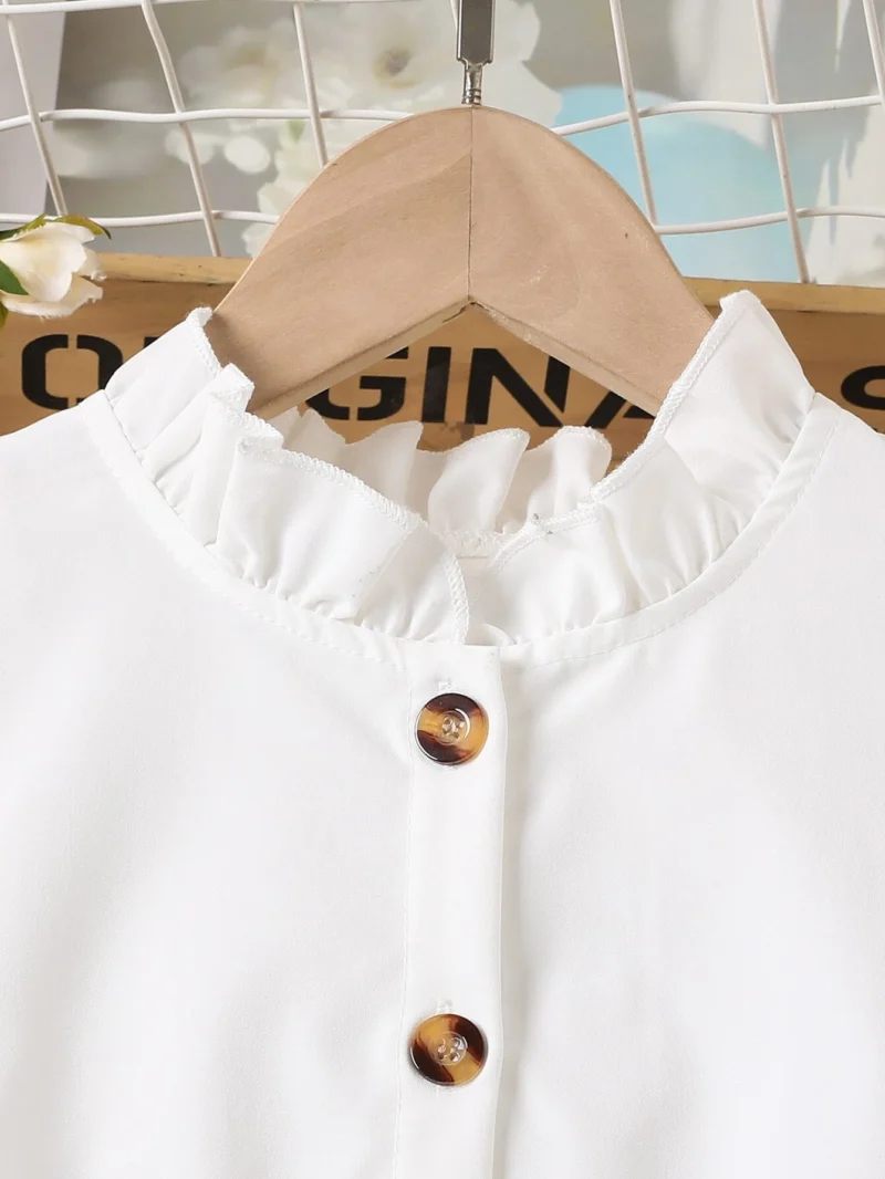 Detalle escote: Detalle de cuello alzado con volantes y botones del vestido blanco con cinturón marrón para niña.
