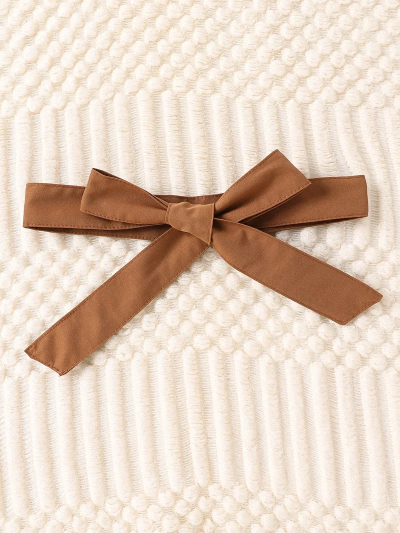Detalle cinturón: Primer plano del cinturón marrón del vestido blanco para niña.