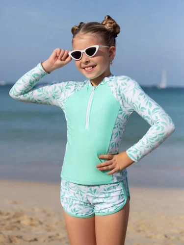 Niña usando set de bañador infantil verde menta con estampado floral en la playa.