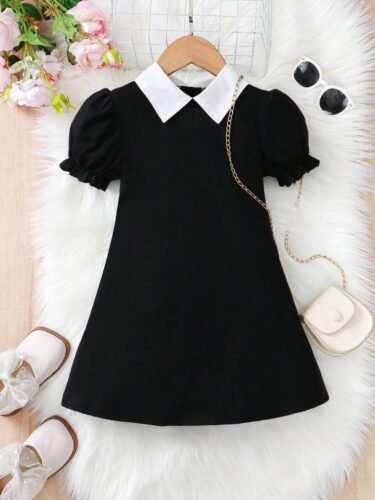 Vestido negro elegante para niñas con cuello camisero y mangas farol, acompañado de accesorios.