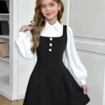Conjunto blanco y negro con blusa de manga larga y vestido negro con botones decorativos.