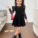 Niña luciendo vestido negro con mangas abullonadas y estampado de corazones.