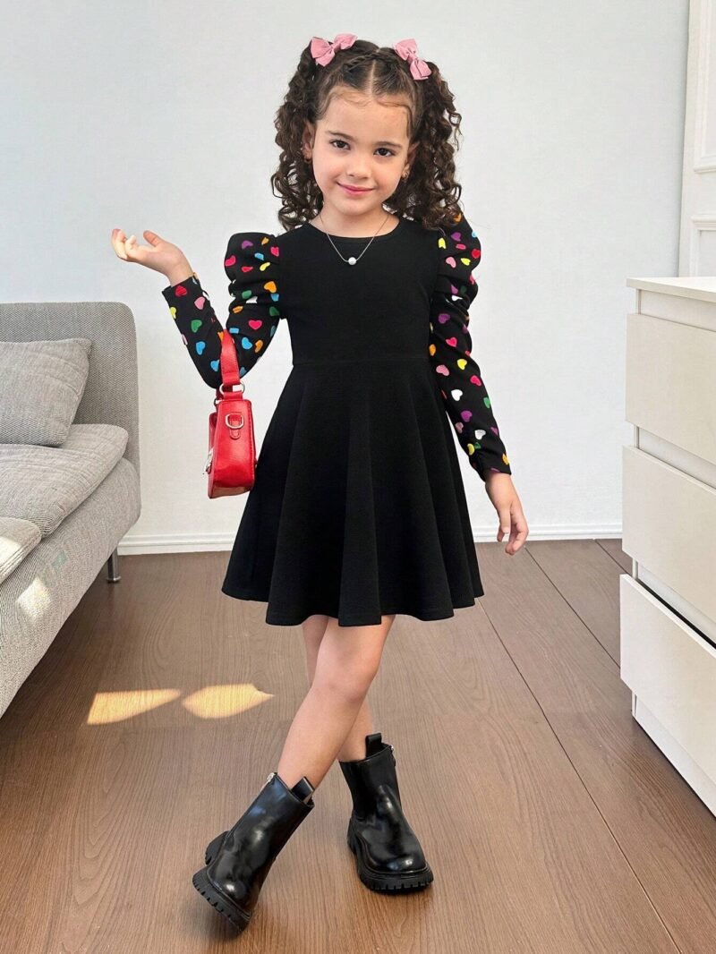 Niña luciendo vestido negro con mangas abullonadas y estampado de corazones.